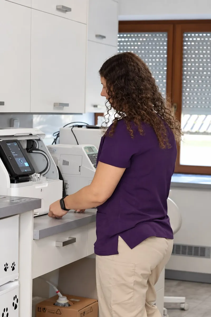 Laborantka ve fialové uniformě pracuje u analyzátorů poblíž okna laboratoře, pohled z boku
